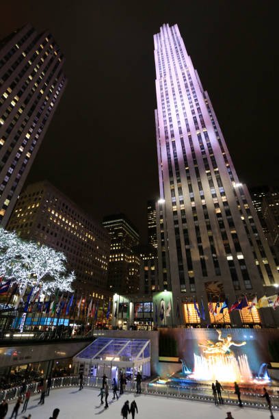 Rockefeller Center Skating Rink in Manhattan, New York City Manhattan, New York City, USA, November 1st, 2014. Night shot showing the Rockefeller Center Skating Rink, the in vibrant colors illuminated fountain and the surrounding skyscrapers. Few people skating on the ice. rockefeller ice rink stock pictures, royalty-free photos & images