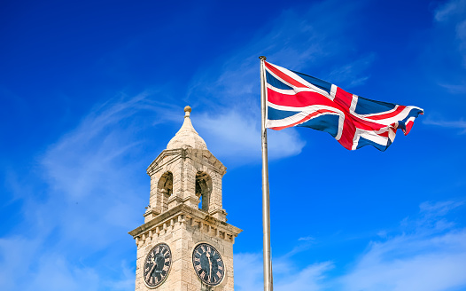 An old stone clock tower and British flag against a cloudy sky