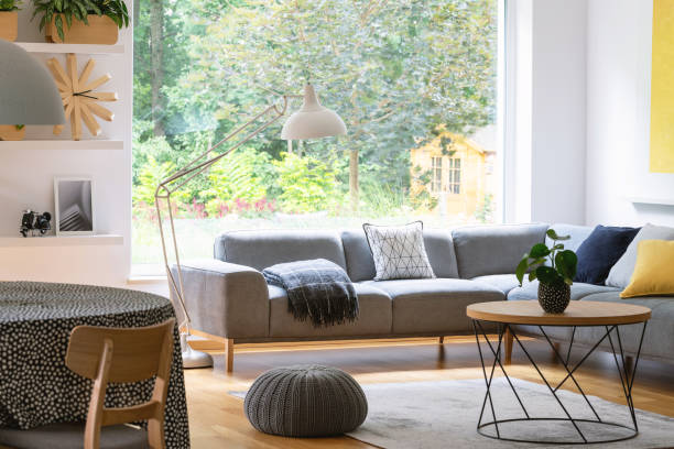 istock Pouf next to table in modern living room interior with grey corner sofa and window. Real photo 1011930008
