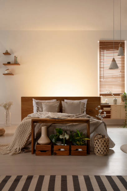 istock Front view of a double bed with pillows and headboard, table and wooden boxes in a natural bedroom interior. Real photo. Place your graphic 1011930948