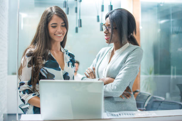 istock Two smiling business women using laptop in office 1011931072