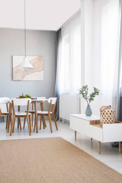 istock White chairs at dining table in scandi flat interior with cupboard, poster and carpet. Real photo 1011935946