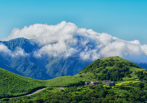 Where: shot at the YangMingShan national park area.\nWhen: a hot summer time hike to cool off with the mountain air.\nWho: a few small specs at the bus stop but they look like tiny specs more or less\nWhy: I noticed the clouds forming over the distance peak and used the long lens to compress the landscape to give it the sense of size.\ndate created: July 9, 2018