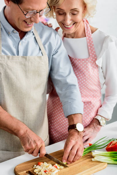 istock smiling senior wife hugging husband while he cutting green onion at kitchen 1011950190