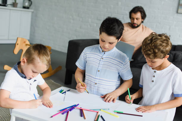 istock kids drawing pictures with colorful pencils while father using laptop on sofa at home 1011955112