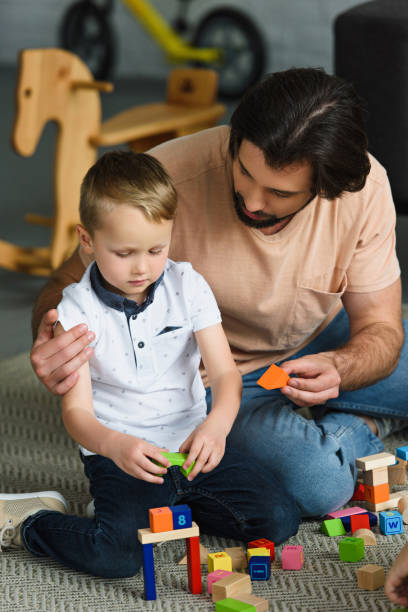 istock father hugging little son while playing with wooden blocks together at home 1011955246