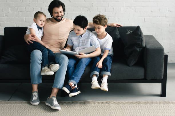 istock smiling father and sons reading book together at home 1011955348