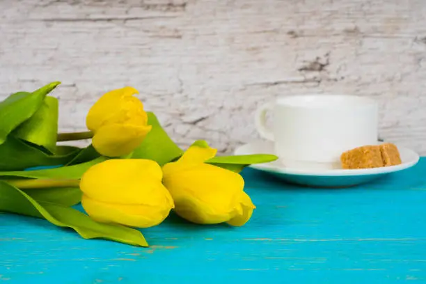 yellow tulips with coffee cup on turquoise wooden table