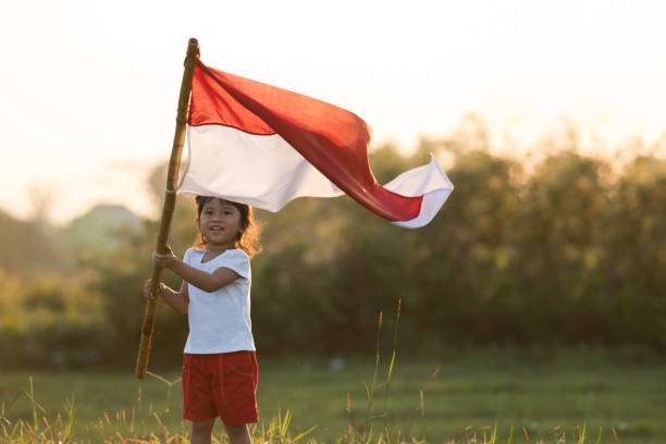 kids raising indonesian flag portrait of kids raising indonesian flag in sunset sky 1945 stock pictures, royalty-free photos & images