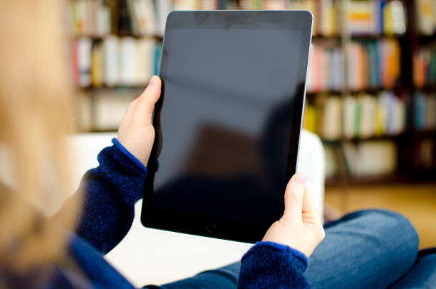 Woman holding blank digital tablet computer with copy space in her hands and looking at the device screen