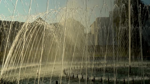 Water jets dance to the music in the city fountain on the background of the yellow sunset in the Park.