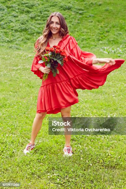 Joven Feliz Hermosa Mujer En Vestido Rojo Bailando Sobre El Pasto Verde Y Con Ramo De Rosas Rojas Foto de stock y más banco de imágenes de Adulto - iStock Joven Feliz Hermosa Mujer En Vestido Rojo Bailando Sobre El Pasto Verde Y Con Ramo De Rosas Rojas Foto de stock y más banco de imágenes de Adulto - iStock