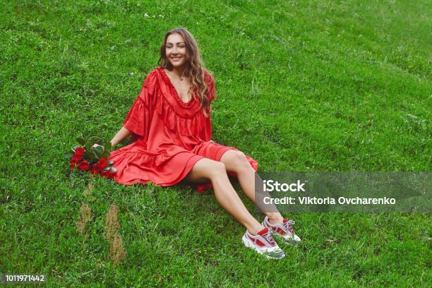 Joven Feliz Hermosa Mujer En Vestido Rojo Sentado En El Pasto Verde Y Con  Ramo De Rosas Rojas Foto de stock y más banco de imágenes de Adulto - iStock