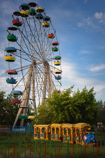 An old colored Ferris wheel and a train ride for children in the city park