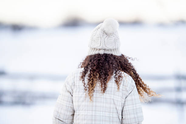 A girl of African descent is outdoors on a winter day. She is looking at a snow-covered field.
