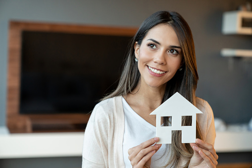 Portrait of a happy woman thinking of buying a house and holding a paper home while smiling - home ownership concepts