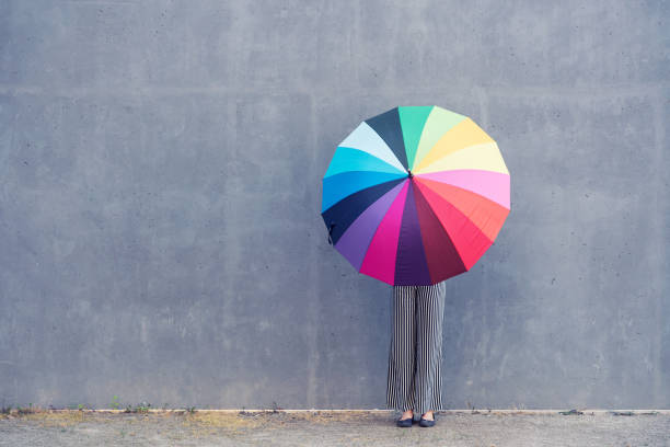 jeune femme debout avec un parapluie multicolor devant un mur de béton - colors color image rainbow umbrella photos et images de collection