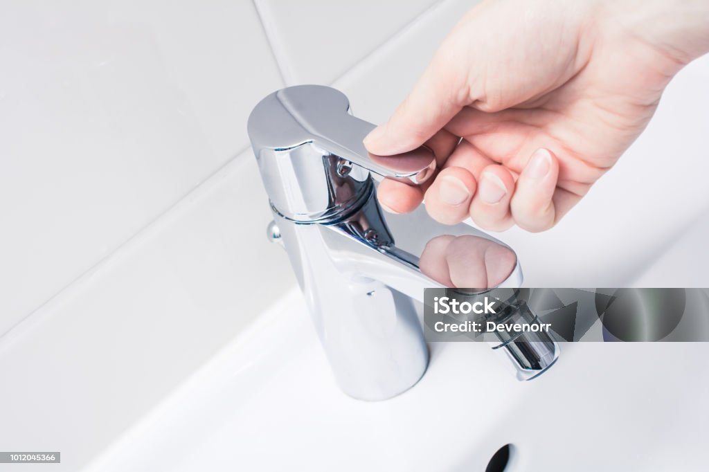 Female Hand On The Handle Of A Chrome Faucet, Ready To Turn On Water A Female Hand On The Handle Of A Chrome Faucet, Ready To Turn On Water Faucet Stock Photo