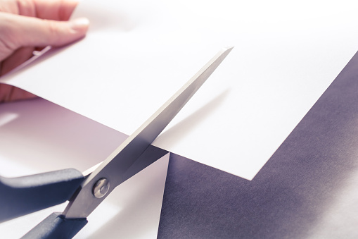 A Pair Of Scissors Cutting White Paper, Holded By Female Hands