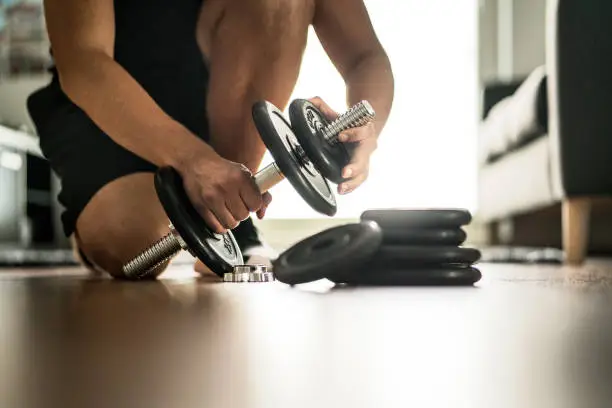 Photo of Improvement and getting stronger in fitness, exercise and muscle training concept. Man adding more weight to adjustable dumbbell in home gym.