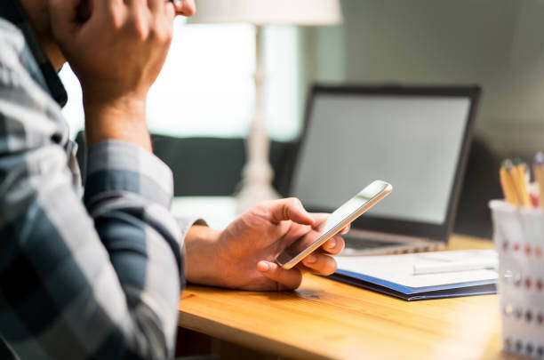 istock Lazy worker using phone in office avoiding work. Bored, sad or unhappy man leaning against hand and browsing social media on internet with smartphone. Inefficient and unproductive employee. 1012049062