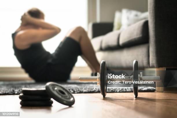 Home Workout Man Doing Ab Training And Crunches In Living Room Gym Guy Doing Sit Ups Warm Up Before Weight Exercise Fitness Concept With Dumbbell Stock Photo - Download Image Now