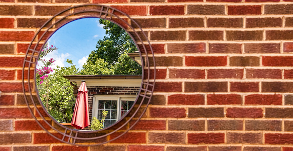 Banner of blurred brick wall with mirror hanging on it reflecting house and patio and trees and blue sky of house with identical brick