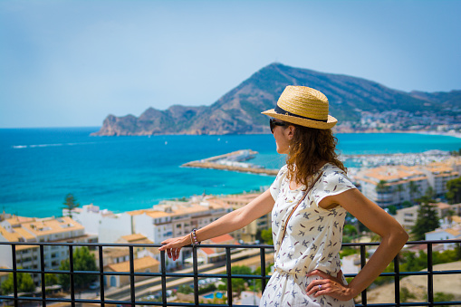 Tourist woman with straw sunhat looking to the mediterranean sea in Altea, Alicante, Spain