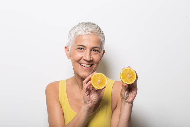 istock Mature woman holding lemon split into two and smiling 1012095930