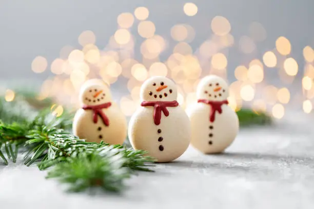 Photo of Sweet macaroons in the form of a snowman. Fir branches on a gray background. Merry Christmas card. New year mood