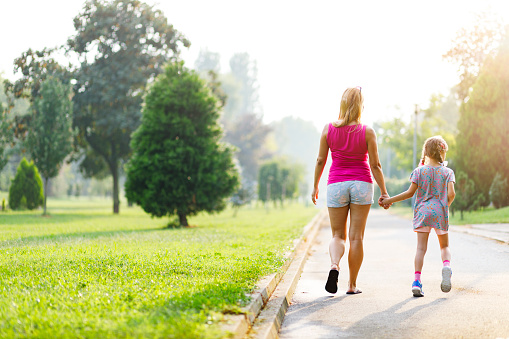 Mother is walking and holding hands with her daughter in the park in summer.