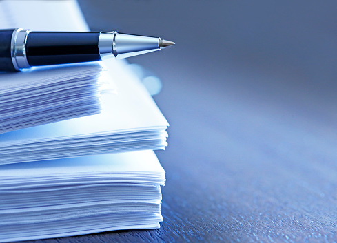 A ballpoint pen rests on top of a stack of documents ready for signing.  The image is photographed using a very shallow depth of field with the focus being on the tip of the pen.