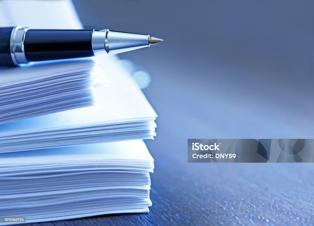 Ballpoint Pen Resting On Top Of Stack Of Documents A ballpoint pen rests on top of a stack of documents ready for signing.  The image is photographed using a very shallow depth of field with the focus being on the tip of the pen. Document Stock Photo