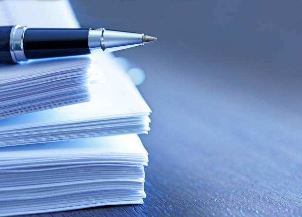 Ballpoint Pen Resting On Top Of Stack Of Documents A ballpoint pen rests on top of a stack of documents ready for signing.  The image is photographed using a very shallow depth of field with the focus being on the tip of the pen. financial report photos stock pictures, royalty-free photos & images