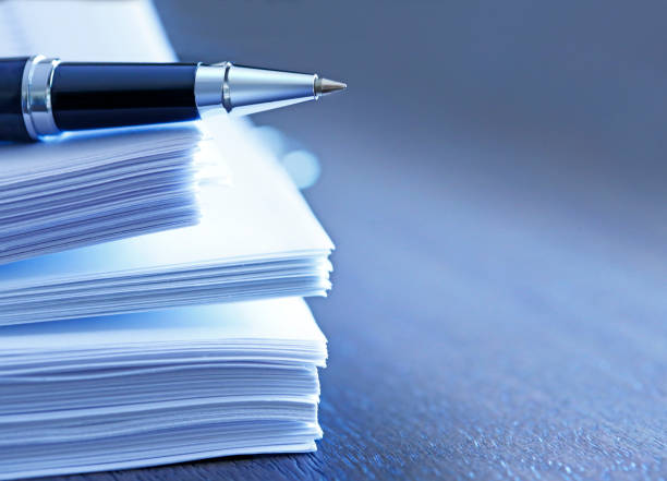 Ballpoint Pen Resting On Top Of Stack Of Documents A ballpoint pen rests on top of a stack of documents ready for signing.  The image is photographed using a very shallow depth of field with the focus being on the tip of the pen. legal document stock pictures, royalty-free photos & images