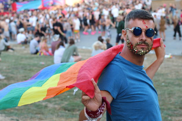 mann mit glitzer bart mit regenbogenfahne - pride lgbtqi veranstaltung stock-fotos und bilder