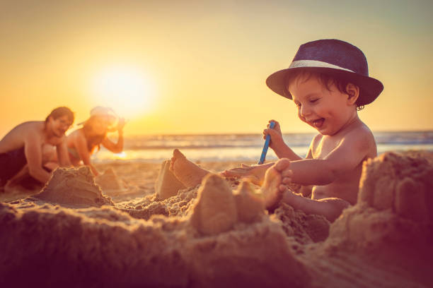 счастливый маленький мальчик здание песчаный замок на пляже - lifestyles child beach digging стоковые фото и изображения