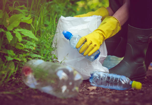 Volunteer in yellow gloves collects plastic garbage