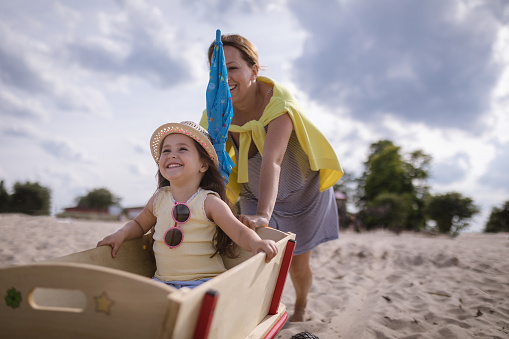 Lovely and cute child with a hat, sitting in a trolley on the beach, enjoying the ride.