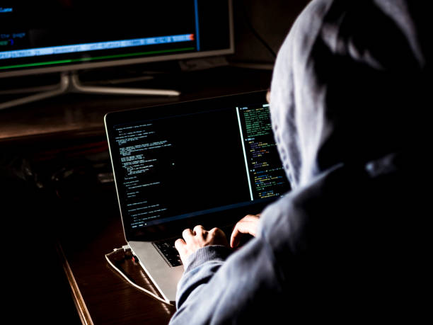 hacker in hoodie typing code in program using laptop in dark studio hacker in hoodie typing code in program using laptop in dark studio east slavs stock pictures, royalty-free photos & images