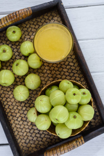 Indian gooseberry in Wooden Tray and juice on white wooden table. Top view