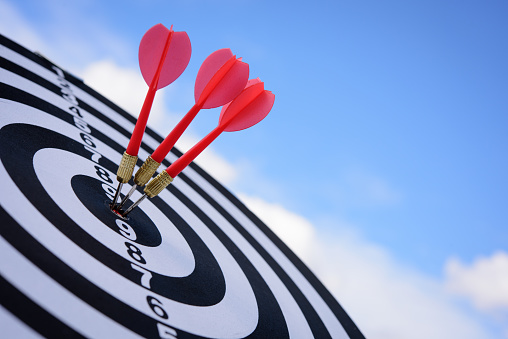 Red dart arrow hitting in the target center of dartboard with blue sky background