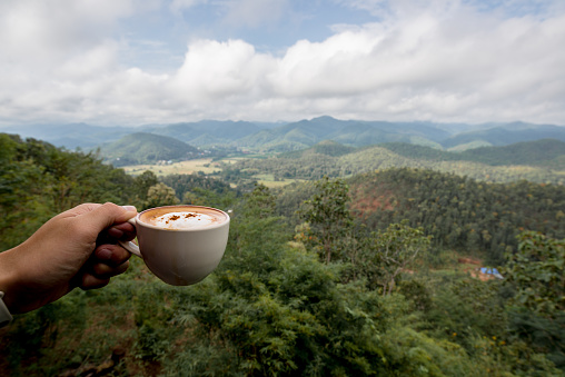 Hot Coffee in a Cup was holding by left hand in front of landscape mountain view, Traveling in Thailand