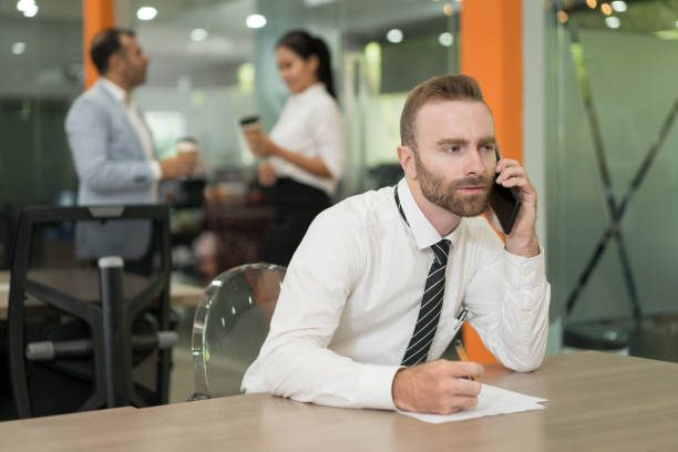 istock Serious young business man talking on phone and working at desk 1012390120