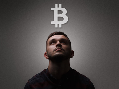Facet portrait a man looking up on bitcoin symbol. Dark lighting portrait bristle men in checkered shirt looks up with his head up on a dark gray background copy space
