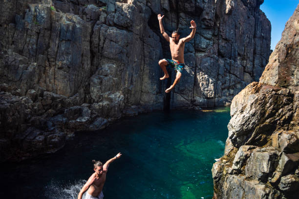 istock Two young men jumping off cliff into sea 1012401686