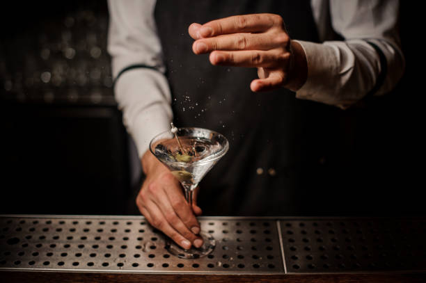 Barman adding salt into a strong martini cocktail Barman adding salt into a strong martini cocktail decorated with a green olive on the bar martini stock pictures, royalty-free photos & images