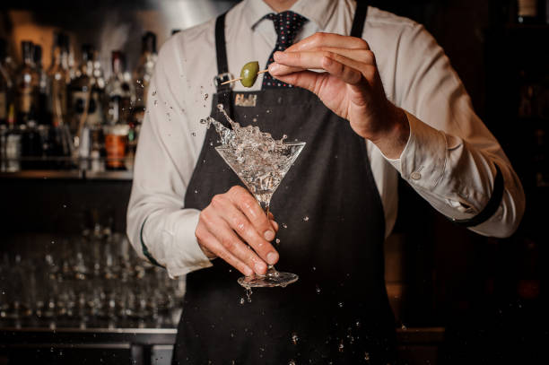 istock Bartender holding a splashing fresh and strong summer martini cocktail with olive 1012429866