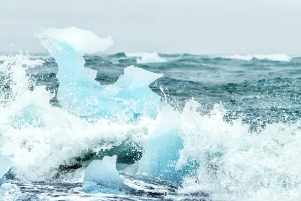 Waves crashing on Jokulsarlon Diamond Ice glacial beach in Iceland against glacier icebergs, splashing water on Atlantic ocean shore during raining, rain storm