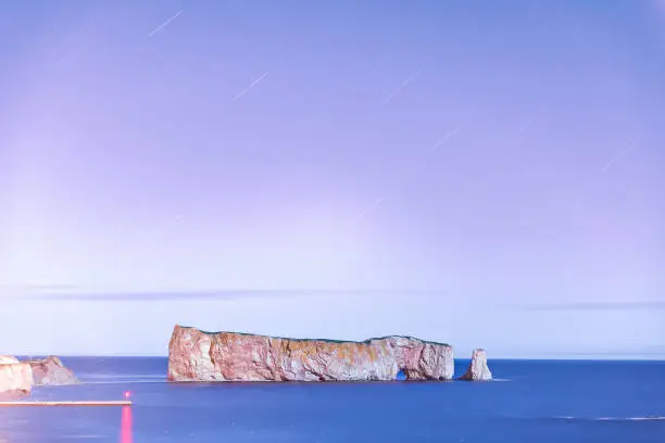 Famous Rocher Perce rock in Gaspe Peninsula, Quebec, Gaspesie region, Canada at dark night starry purple sky, stars at Saint Lawrence gulf, wharf, dock, pier, lighthouse, reflection